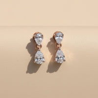 Teardrop-shaped earrings held between fingers with a Christmas tree background