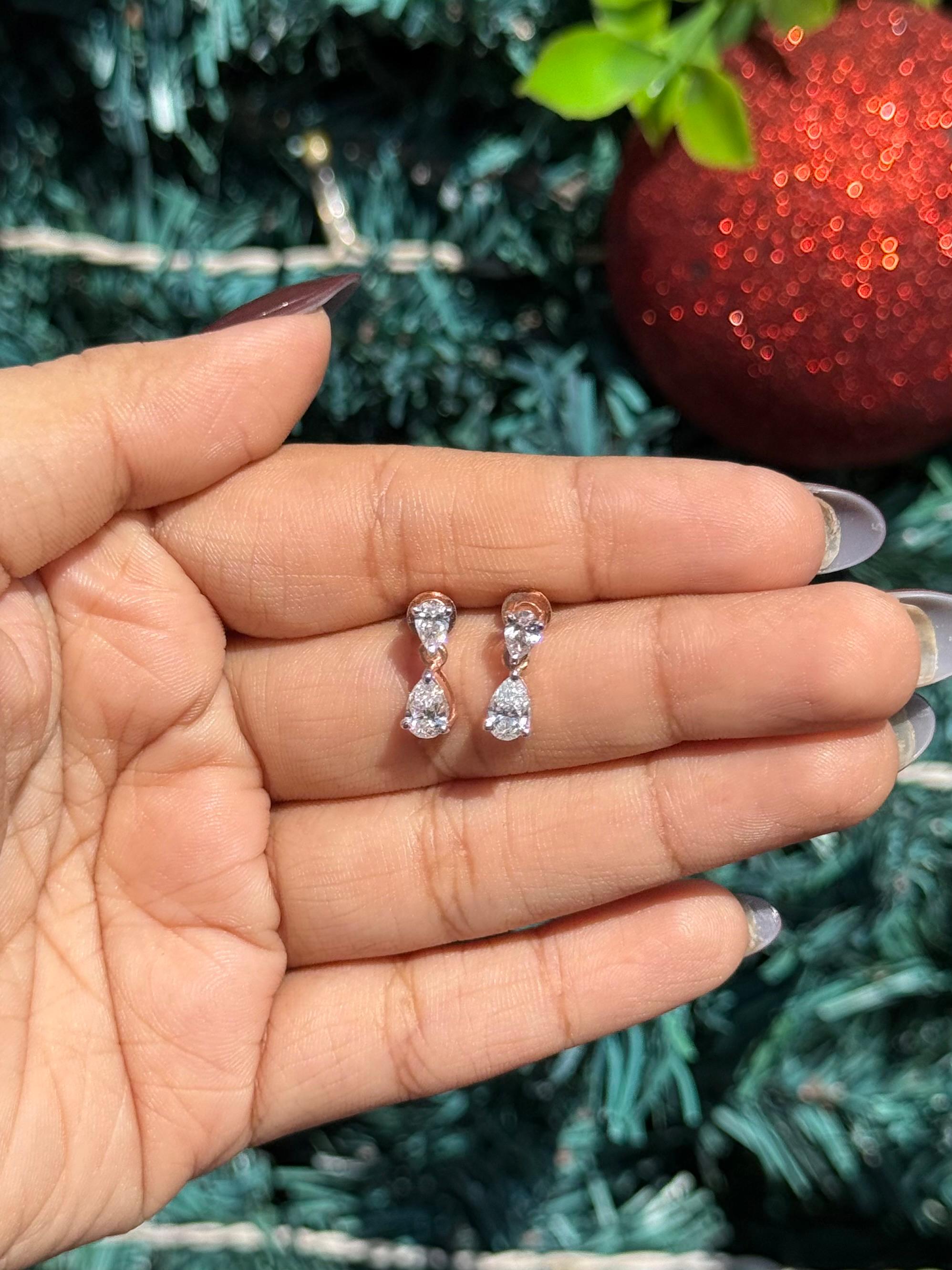 Teardrop-shaped earrings held between fingers with a Christmas tree background